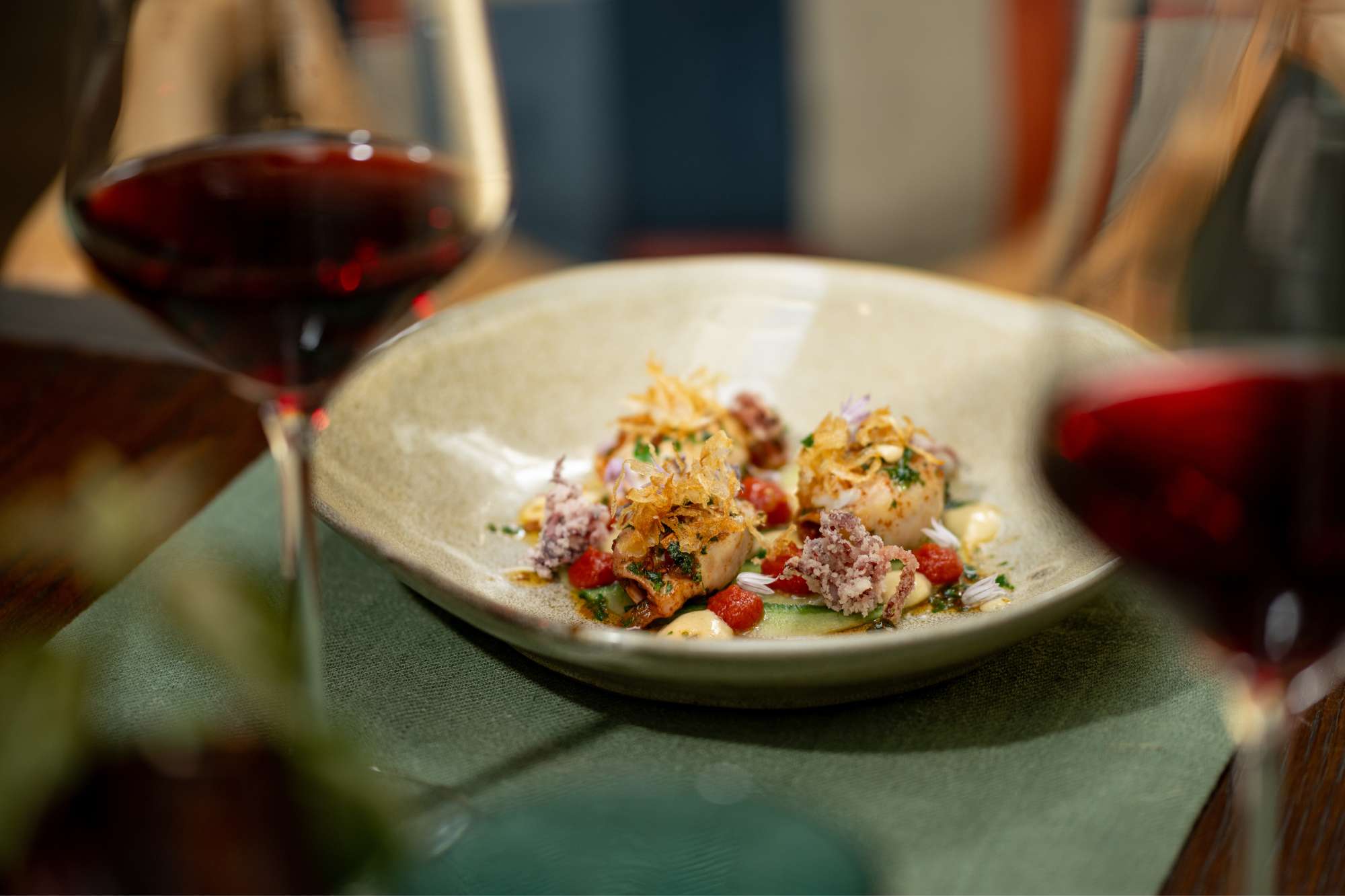 2 | Vineyard Hotel Plate of small savory bites with crispy topping and colorful garnish, accompanied by a glass of red wine in a warm dining setting.