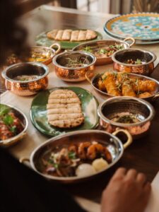 Copper serving bowls filled with assorted Indian dishes on a dining table, including flatbread on a green plate in the center.
