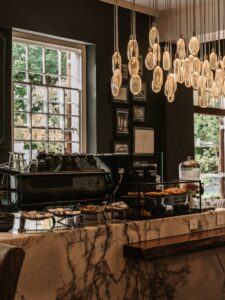 Cafe interior with marble counter, pastry display, and clustered glass pendant lights above the bar area.